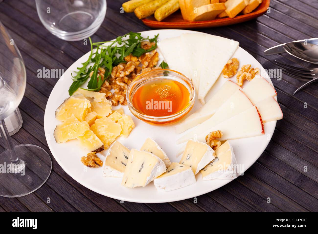 Assiette de fromage avec différents types de délicieux fromages garnis de miel, de noix et d'arugula Banque D'Images