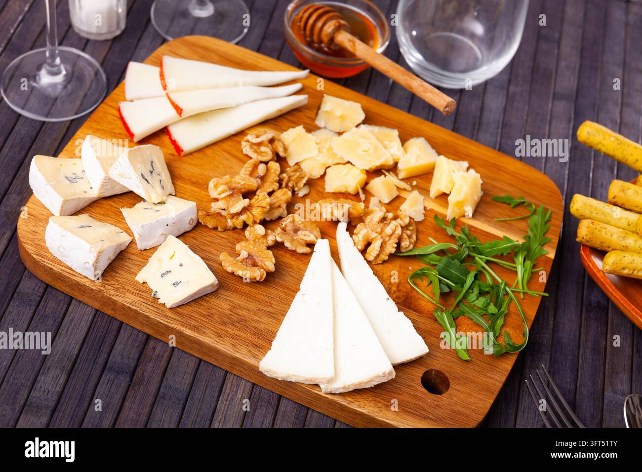 Différents types de fromage tranché servis sur une planche à découper en bois avec du miel et des noix Banque D'Images