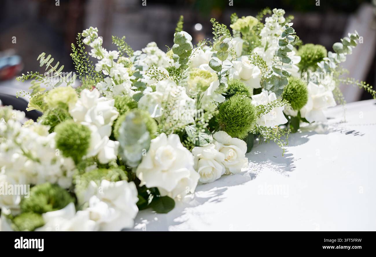 Arrangement floral élégant de roses blanches et de verdure sur une voiture de mariage blanche Banque D'Images