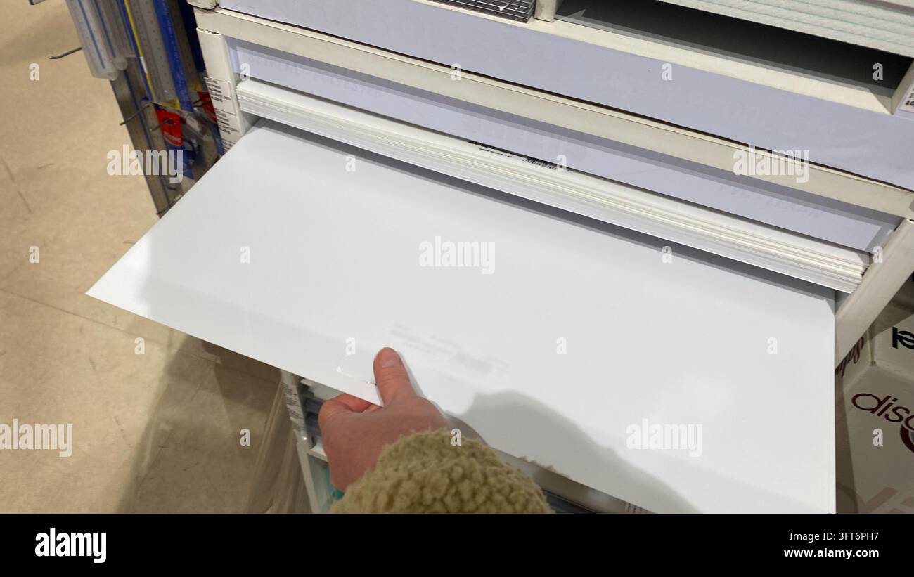 Gros plan de la main d'un client sélectionnant une feuille de papier vierge pour affiche dans un présentoir d'une boutique d'art Banque D'Images