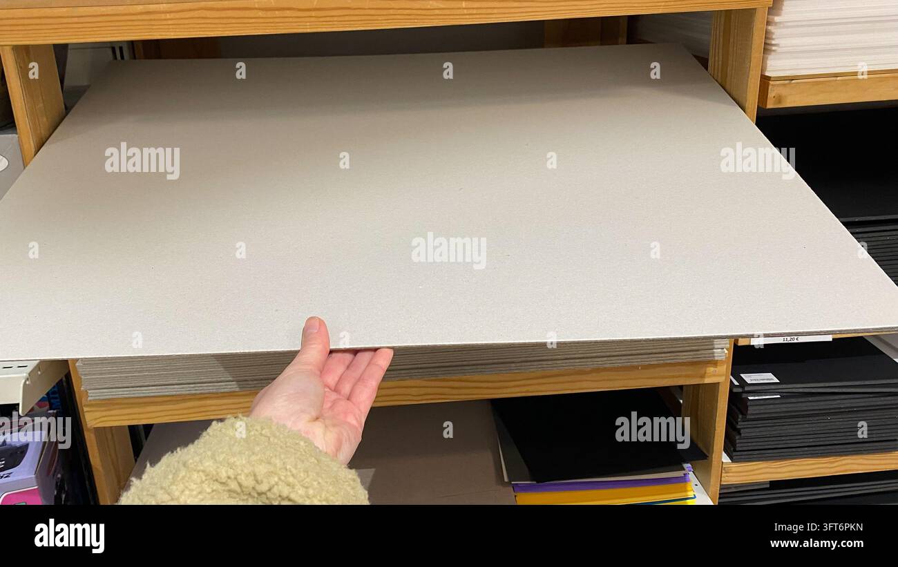 Close-up de la main d'un client sélectionnant une grande plaque de carton gris dans une pile sur des étagères en bois dans un magasin de fournitures artistiques Banque D'Images