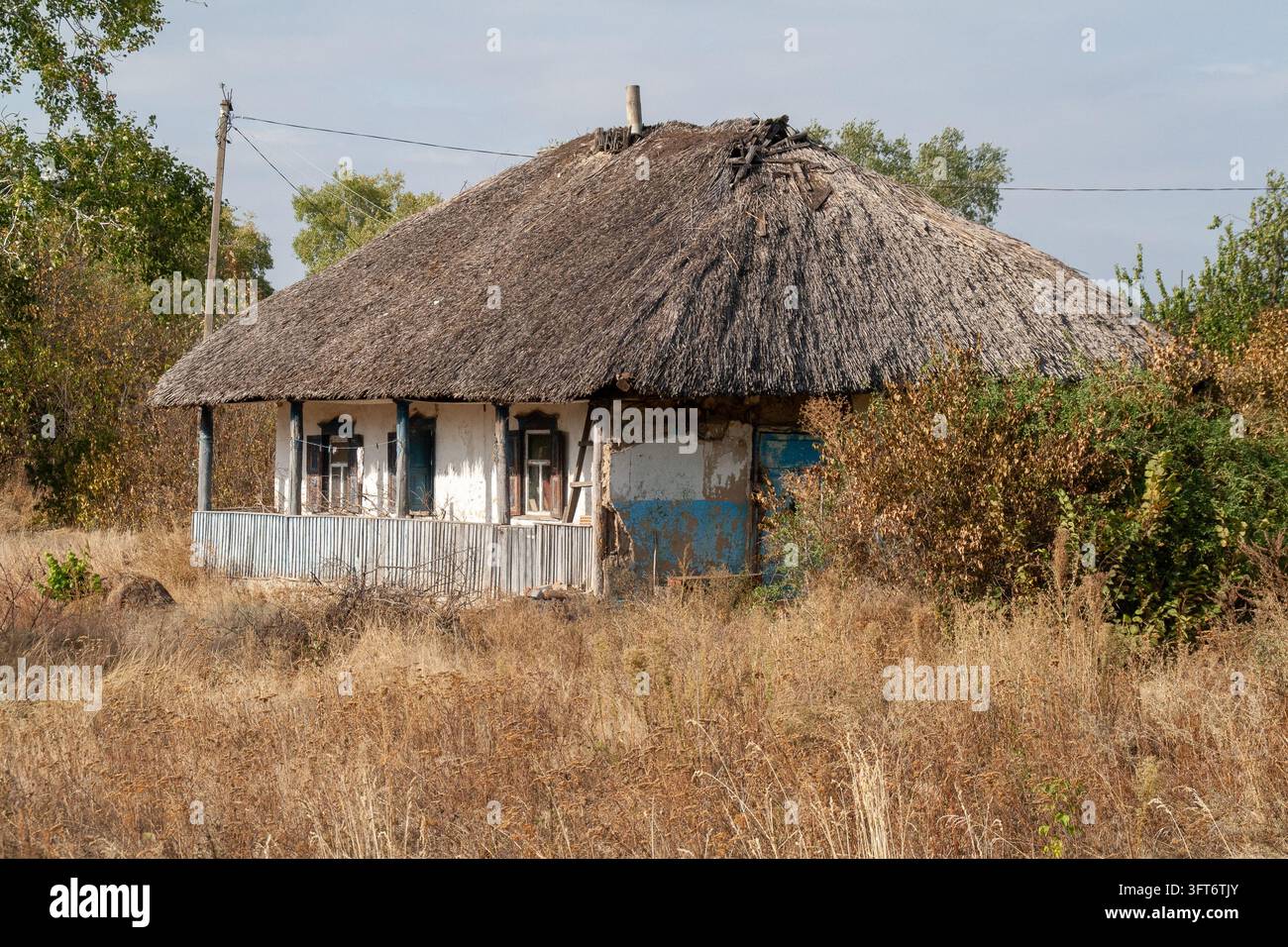 Hutte en terre traditionnelle ukrainienne au toit de chaume avec des accents bleus dans un paysage rural Banque D'Images
