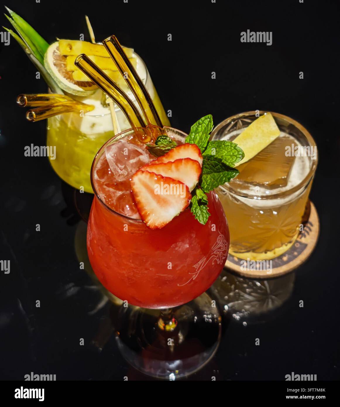 Trois cocktails fruités colorés avec des garnitures de fruits frais sur une table de bar sombre Banque D'Images