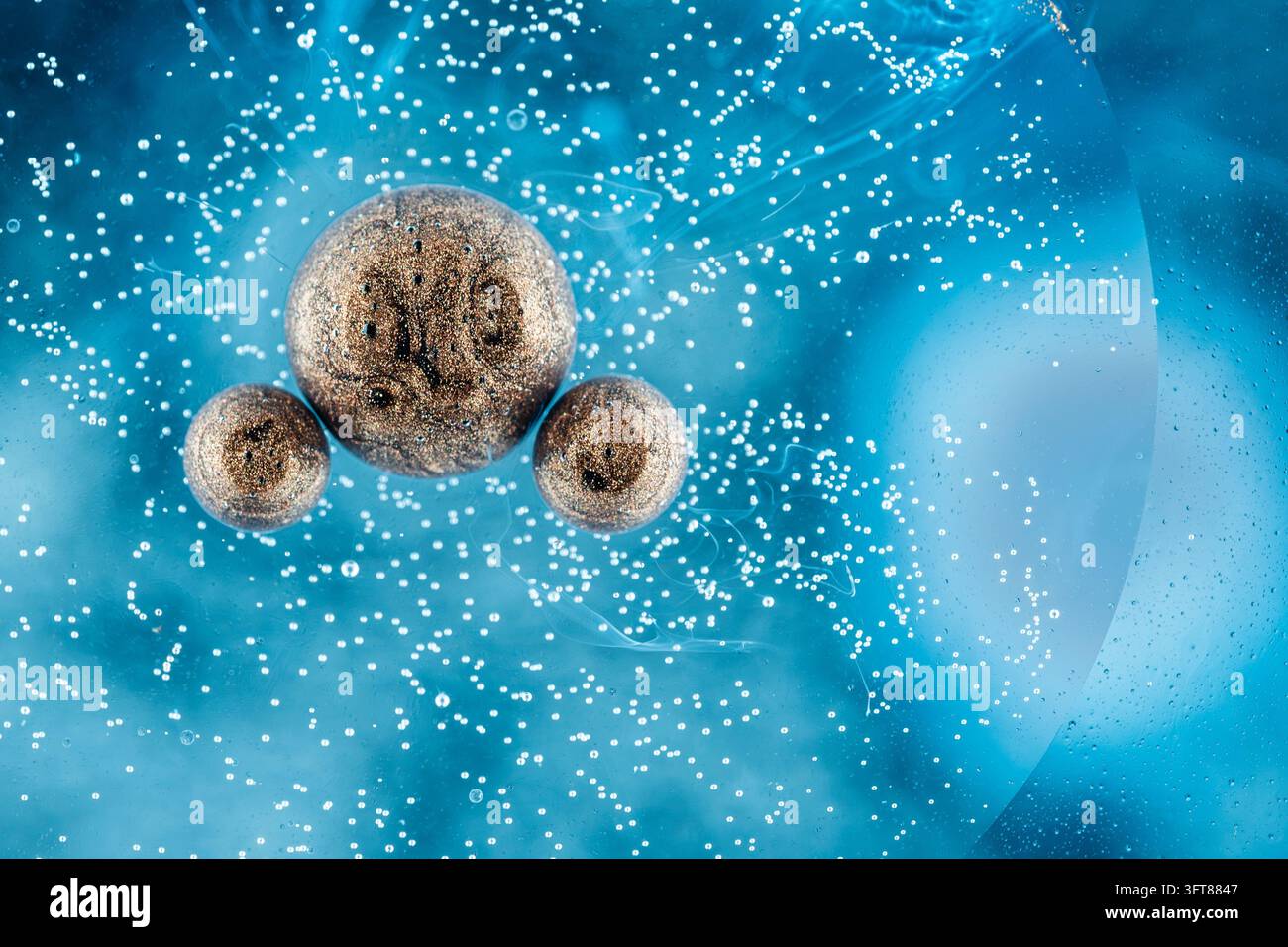 Vue macro de sphères brunes étincelantes flottant dans une huile bleue vibrante et de l'eau, entourées de minuscules bulles et de paillettes Banque D'Images