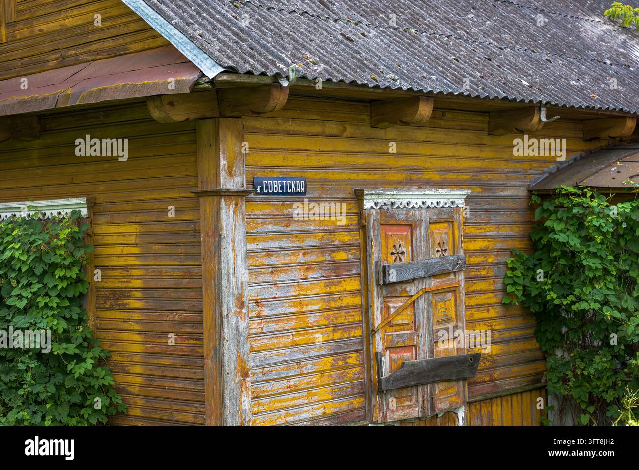 Structure résidentielle en bois délabrée avec peinture ocre jaune, toit en métal et panneau de rue de l'ère soviétique. Banque D'Images