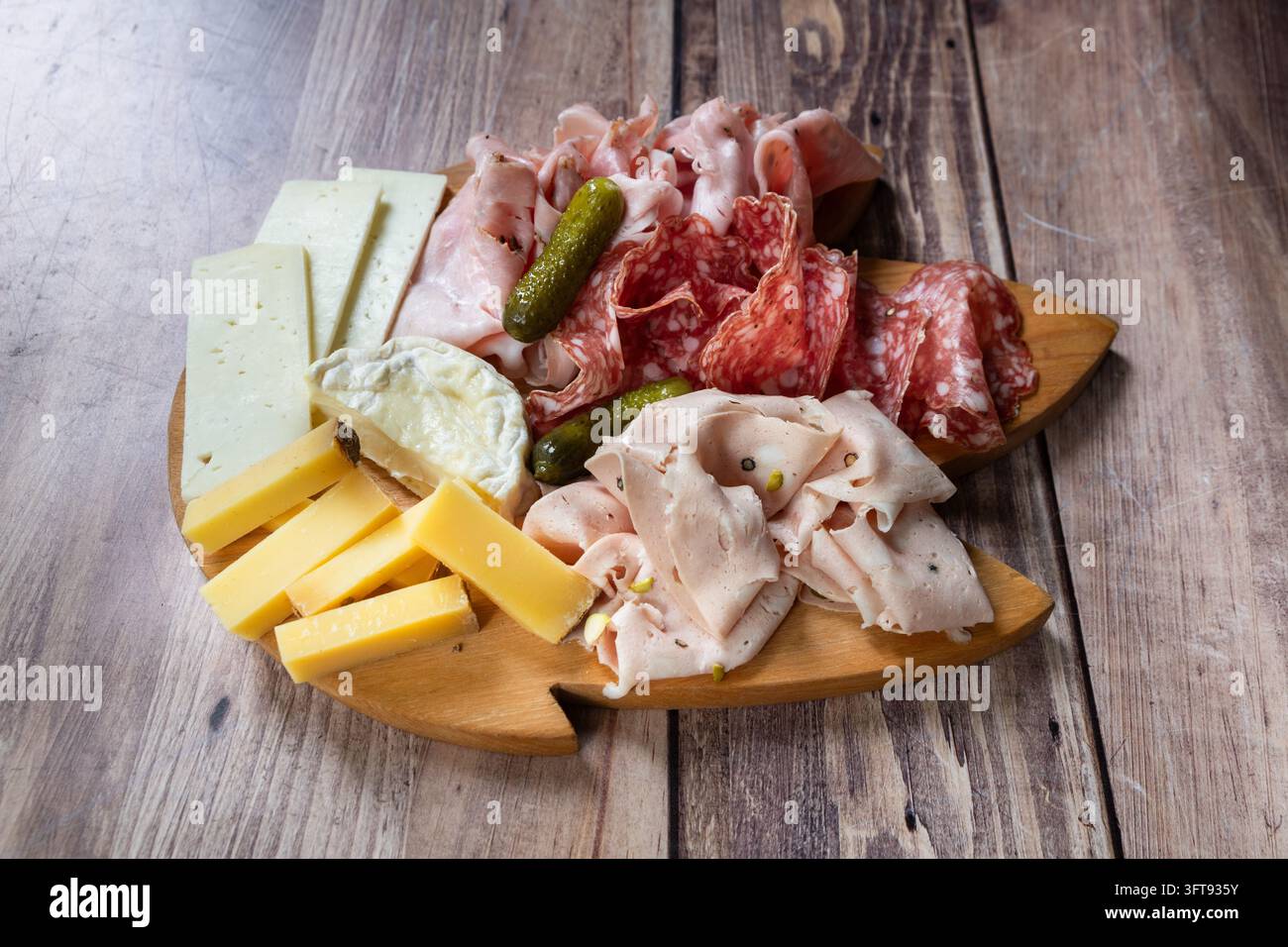 Diverses charcuteries tranchées, salami et fromages accompagnés de cornichons disposés sur une planche de service en bois. Banque D'Images