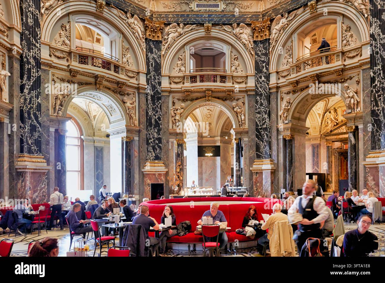 Invités et serveurs sur des banquettes rouges sous des colonnes de marbre, des arches sculptées et des galeries du café du Musée des Beaux-Arts à Vienne, Autriche Banque D'Images