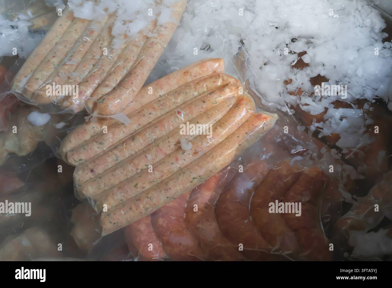 Saucisses assaisonnées emballées sous vide refroidissant dans un bain d'eau glacée lors de la transformation alimentaire. Banque D'Images