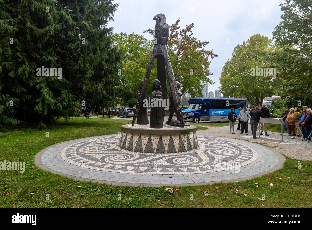 Vancouver, Canada – 7 septembre 2026 : Vue horizontale large sur les touristes à côté d’un bus touristique bleu admirant la sculpture en bronze des Salish de la côte sur un ornementé Banque D'Images