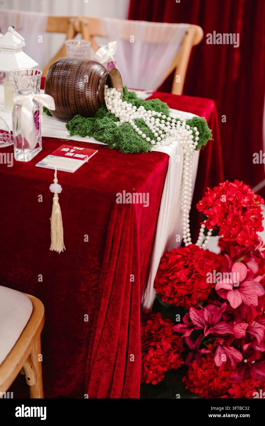 Disposition de table en velours rouge avec pot en argile renversant un collier de perles et des hortensias rouges Banque D'Images