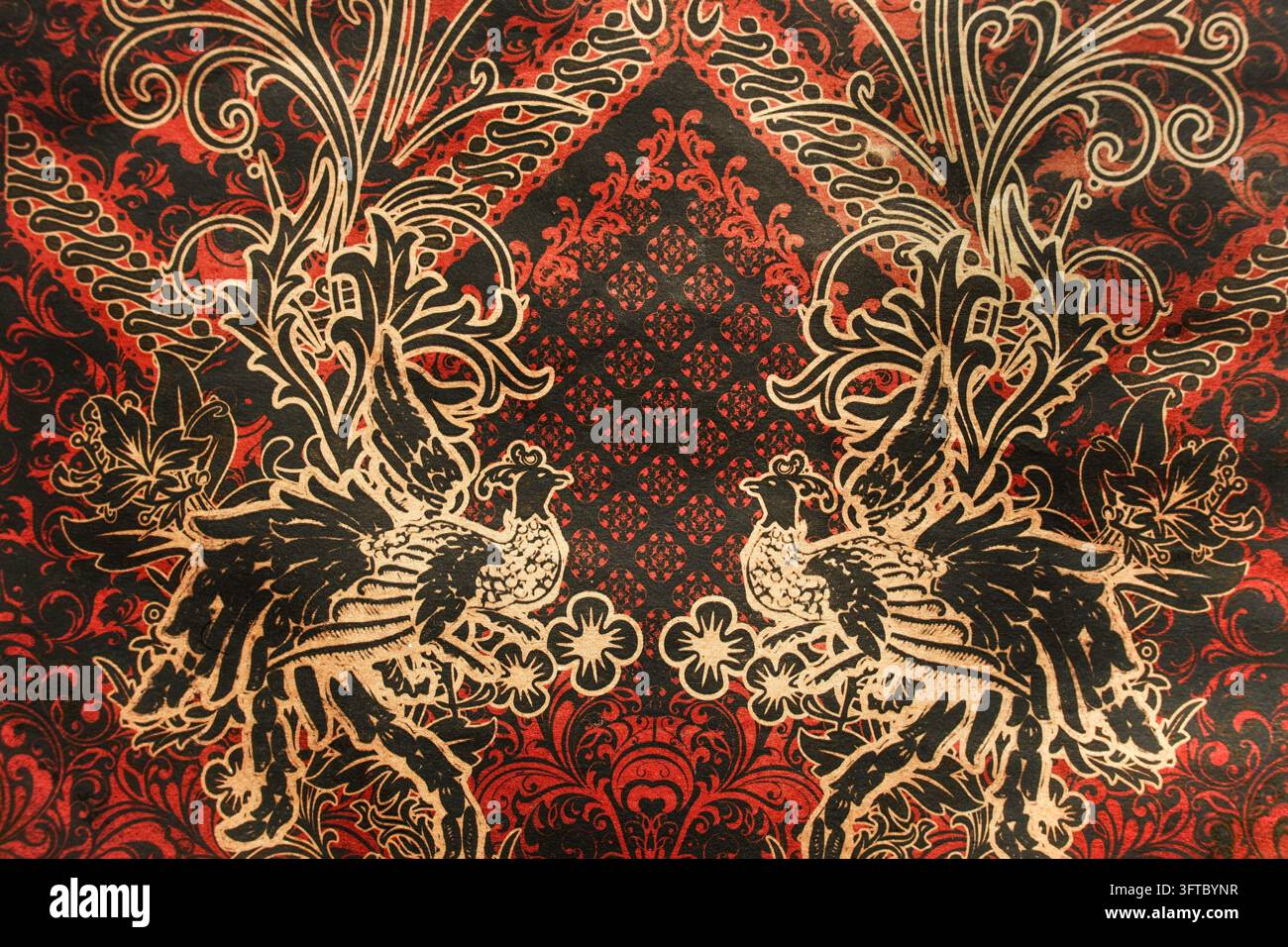 Motif traditionnel de tissu batik indonésien avec ornement élégant d'oiseaux jumeaux or et rouge Banque D'Images