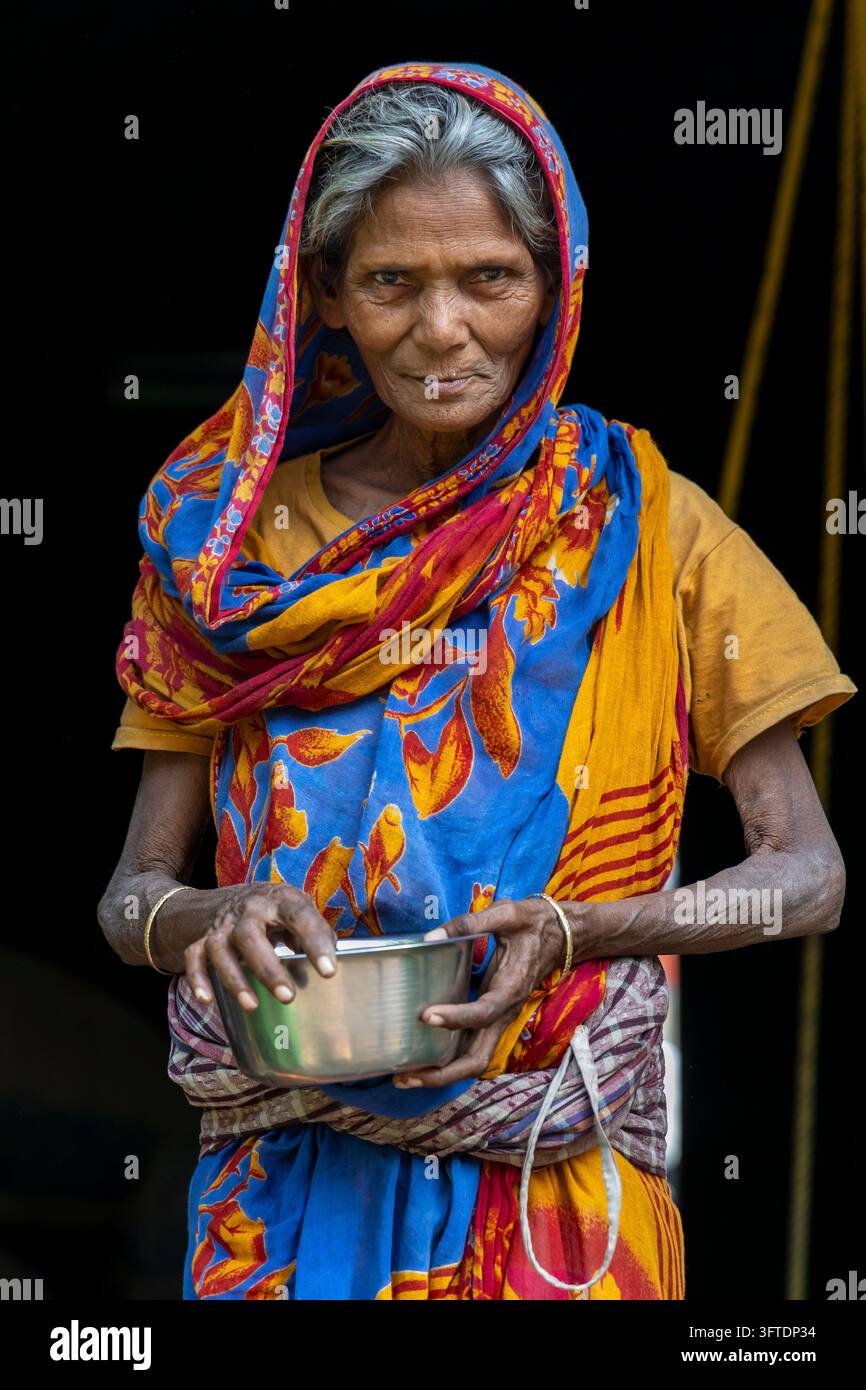 Portrait d'une femme aux cheveux gris avec un couvre-chef bleu et orange tenant un bol d'aumônes en métal à deux mains, Bengale occidentale, Howrah, Inde Banque D'Images