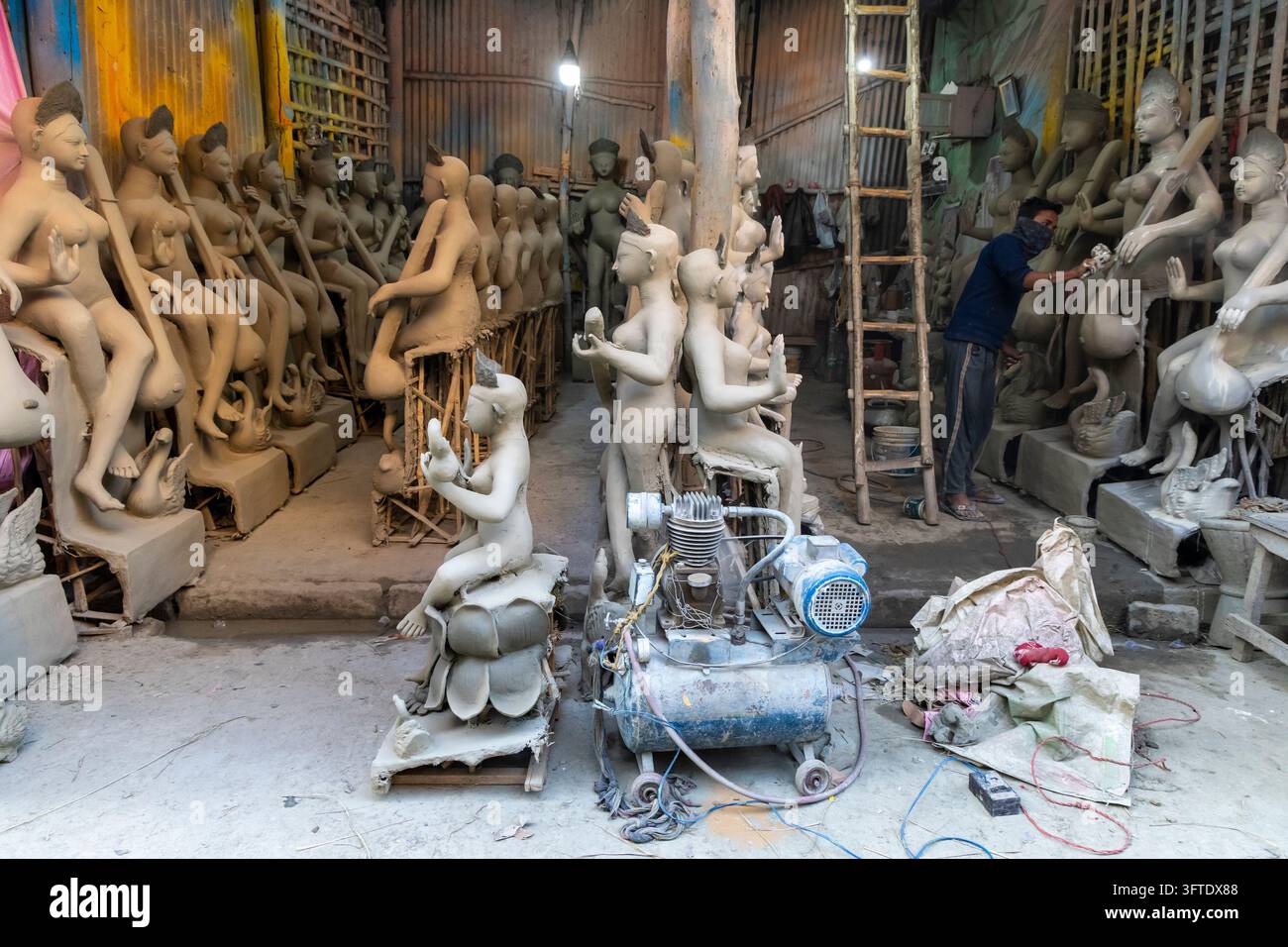 Passage sombre bordée de statues non peintes sur des piédestaux où un homme se tient près d'une échelle haute dans le quartier de Kumartuli, Bengale occidentale, Kolkata, Inde Banque D'Images