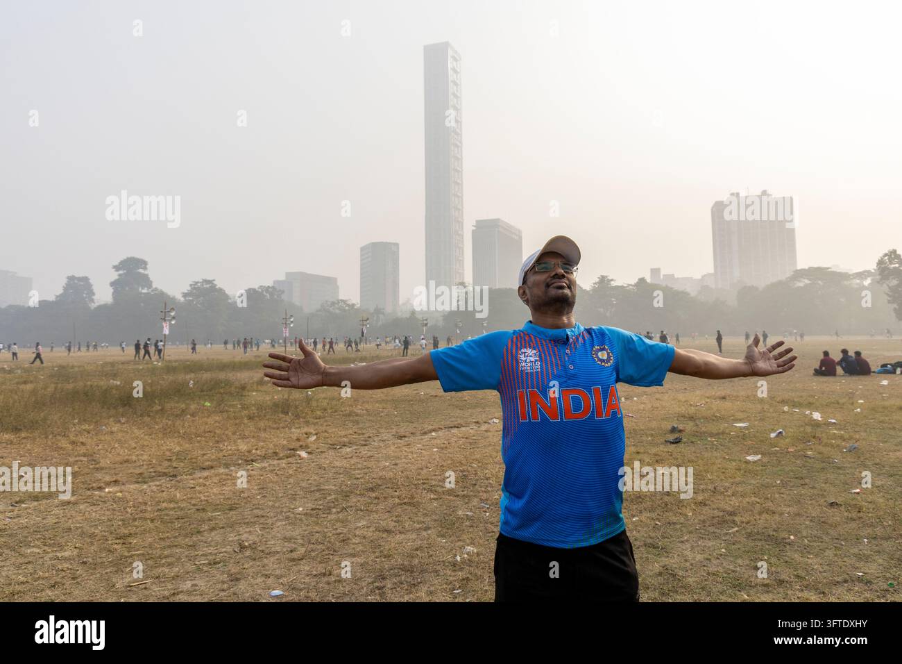 Fan souriant portant un maillot de cricket bleu et une casquette, les bras grands ouverts sur un grand terrain de parc, Bengale occidentale, Kolkata, Inde Banque D'Images