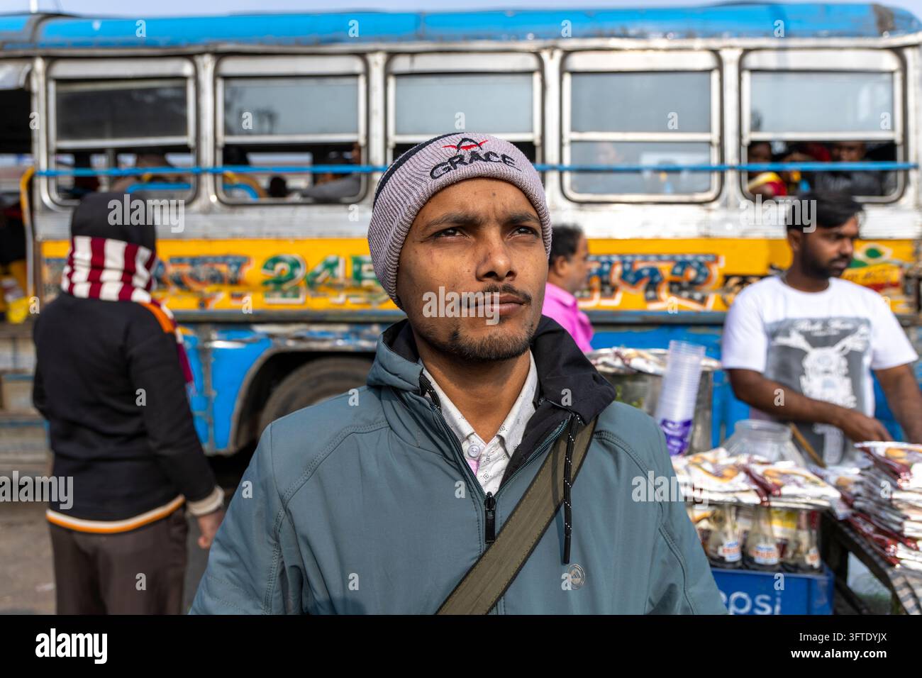 Un homme à la barbe courte portant une veste bleue et une casquette en laine regarde vers le haut et au loin tandis qu'un vendeur se tient derrière un chariot de snacks, Bengale occidentale, Kolkata, Inde Banque D'Images