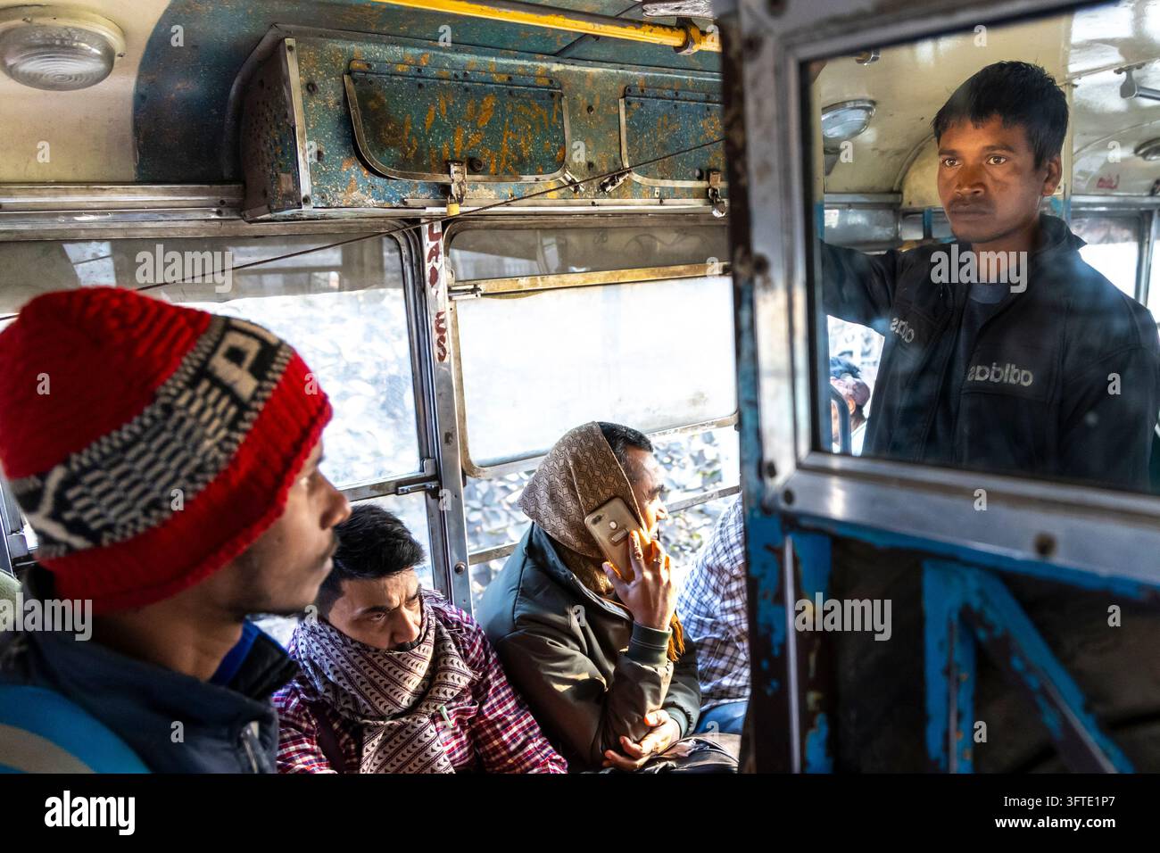 Intérieur d'un bus bleu rouillé où des voyageurs sont assis près des fenêtres avec un homme portant une casquette tricotée rouge regardant à l'extérieur, Bengale occidentale, Kolkata, Inde Banque D'Images
