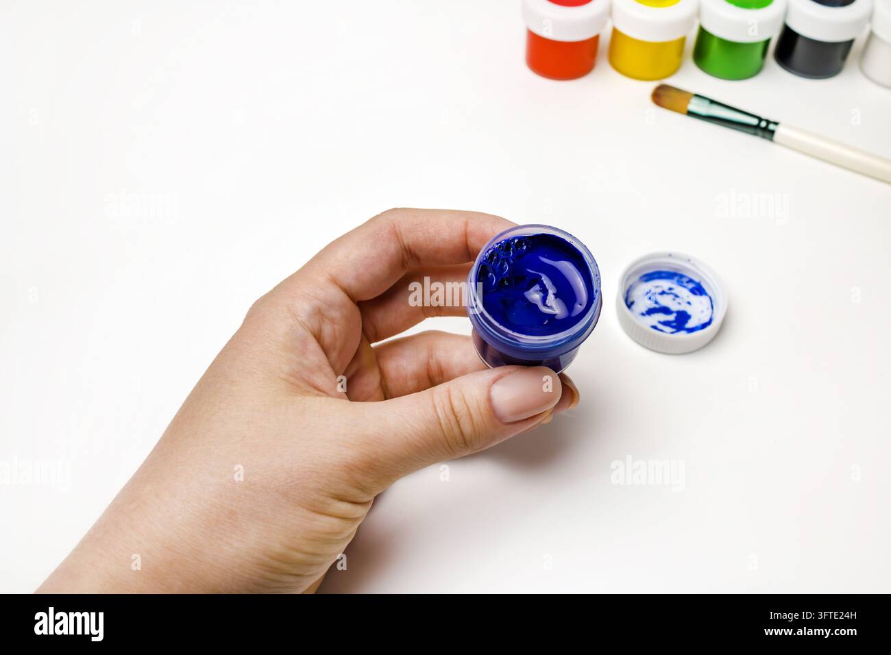 Main féminine tenant un pot de peinture gouache bleue, concept de dessin Banque D'Images