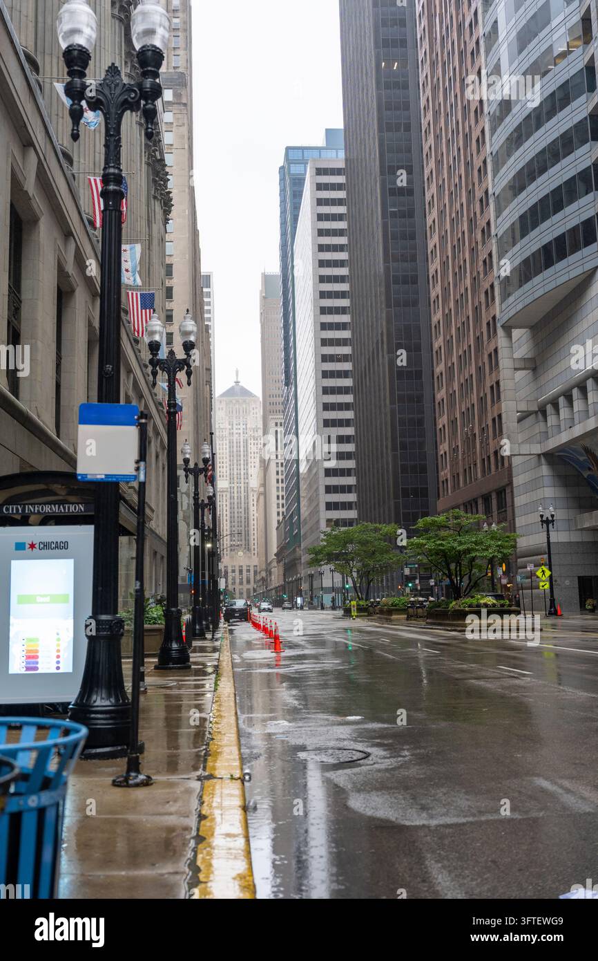 Rue trempée par la pluie dans le centre-ville de Chicago, Illinois, États-Unis, entourée de grands immeubles de bureaux et d'architecture historique. L'asphalte mouillé reflète les lumières de la ville Banque D'Images