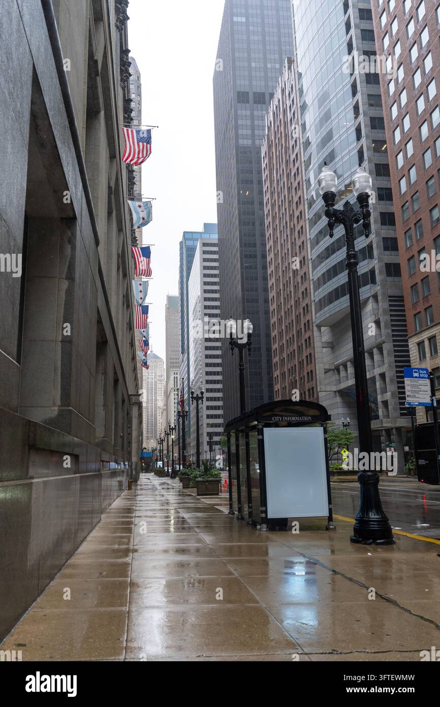 Trottoir mouillé désert dans le centre-ville de Chicago, Illinois, États-Unis, après la pluie. Des drapeaux américains et de la ville de Chicago sont suspendus le long d’un bâtiment historique, avec gratte-ciel Banque D'Images