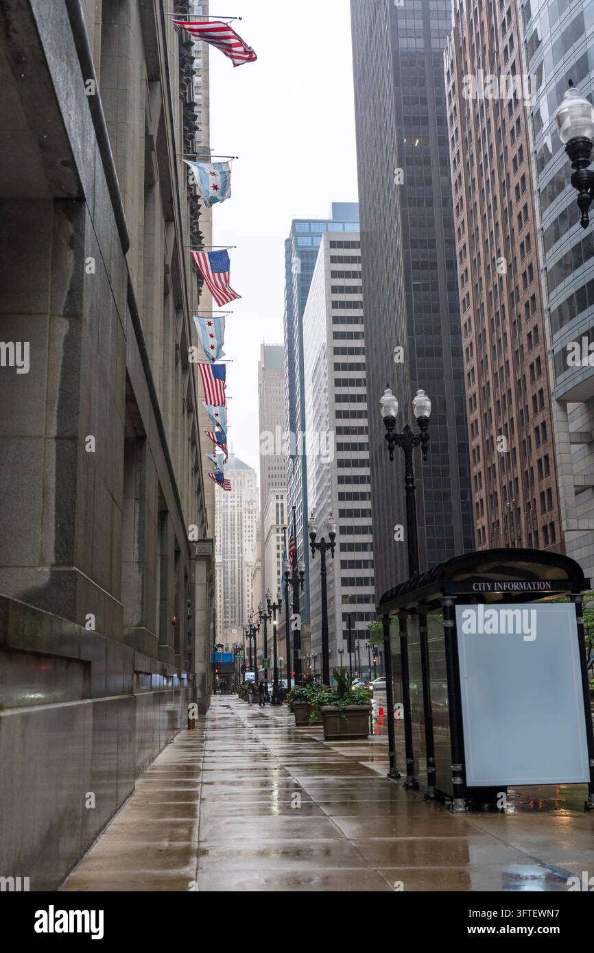 Trottoir mouillé désert dans le centre-ville de Chicago, Illinois, États-Unis, après la pluie. Des drapeaux américains et de la ville de Chicago sont suspendus le long d’un bâtiment historique, avec gratte-ciel Banque D'Images