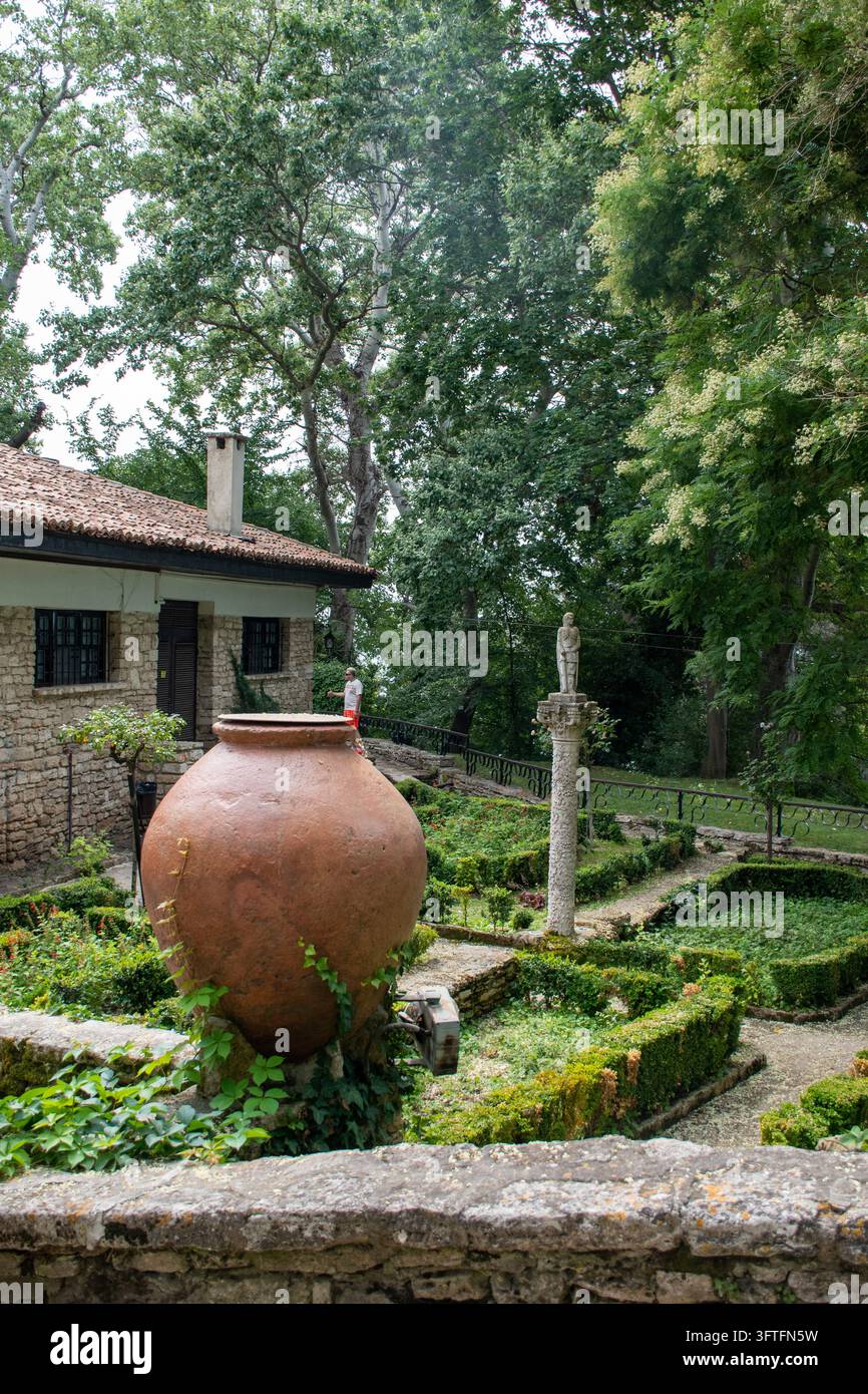 Prise verticale d'une urne amphore en terre cuite antique debout dans une cour de jardin verdoyante. Banque D'Images
