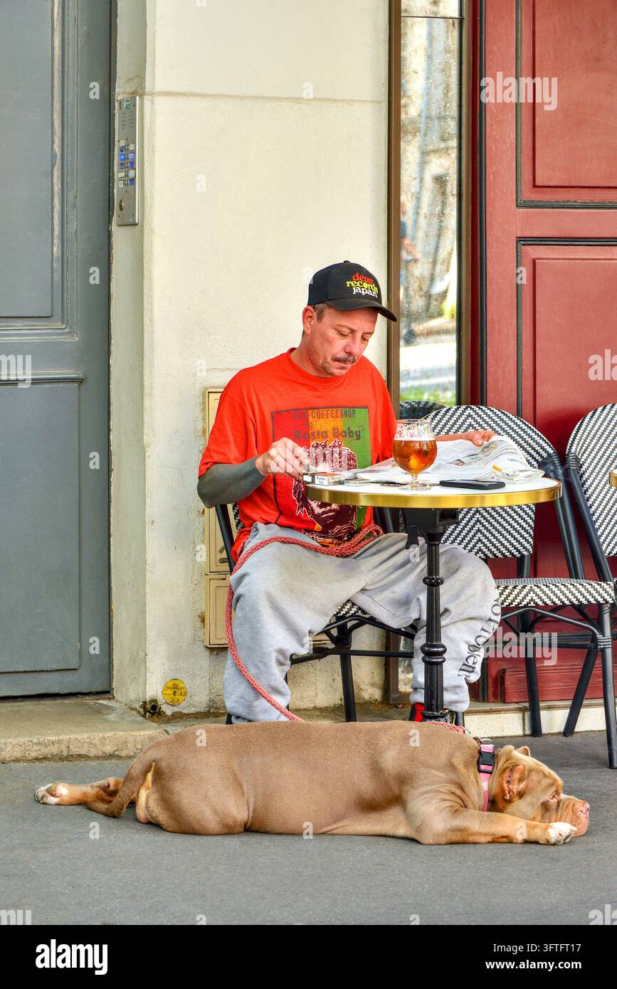 Homme habillé de manière décontractée à une table de café en plein air avec un grand chien Bullmastiff en laisse - Tours, Indre-et-Loire (37), France. Banque D'Images