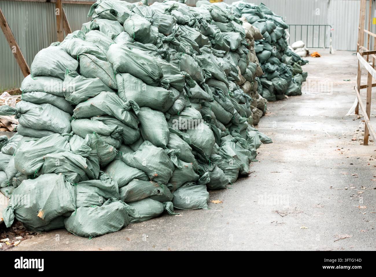 De grandes piles de sacs de sable verts bordent un chemin sur un chantier de construction, servant de barrière temporaire contre les inondations et de mesure de protection contre l'eau et les débris Banque D'Images