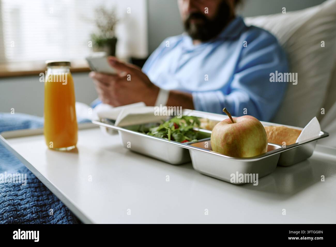 Homme d'âge moyen utilisant un smartphone avec un plateau repas dans un lit d'hôpital Banque D'Images