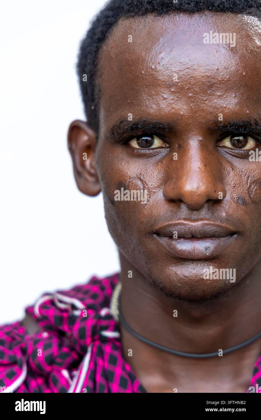 Portrait rapproché d'un homme Maasai portant des marques de scarification circulaires sur les joues, vêtu d'un tissu à carreaux rose et noir, Stone Town, Tanzanie Banque D'Images
