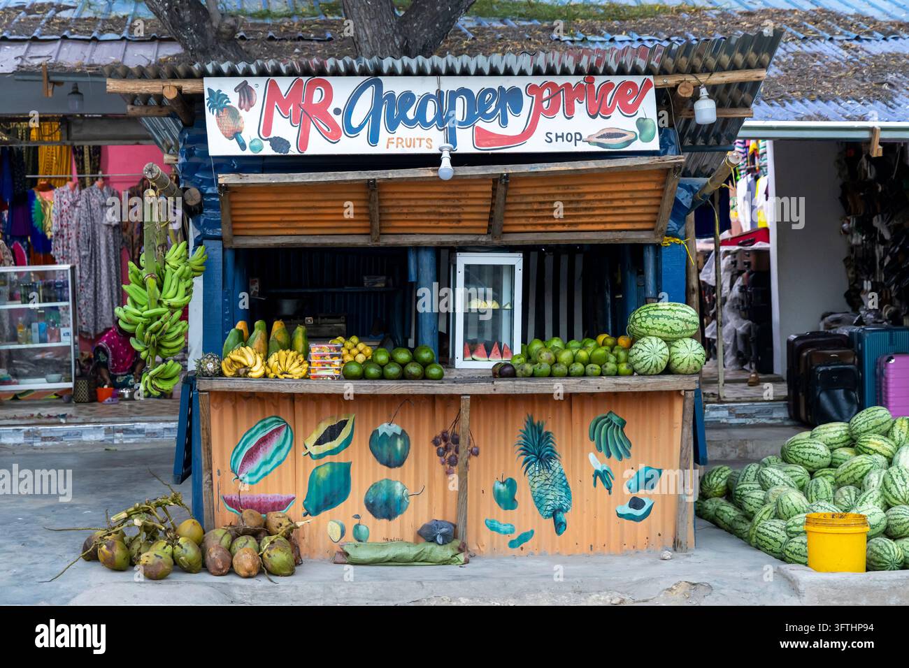 Étal de fruits coloré au bord de la route appelé Mr Cheaper Price avec des murs ondulés et des bananes, des pastèques, des papayers et des noix de coco, Nungwi, Tanzanie Banque D'Images