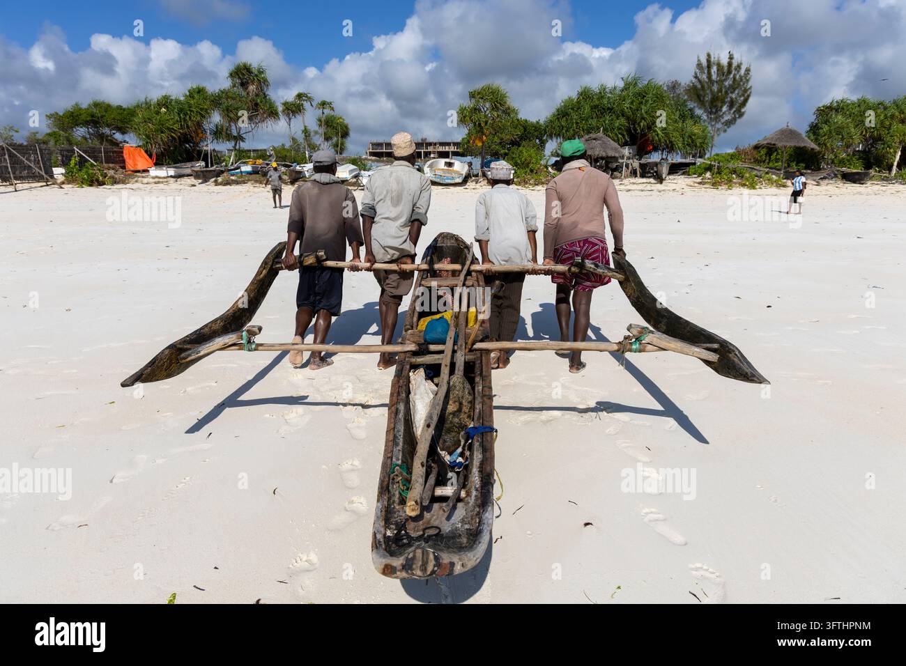 Quatre pêcheurs portant une pirogue traditionnelle en bois sur une plage de sable blanc vue de dos avec de longues ombres, Matemwe, Tanzanie Banque D'Images