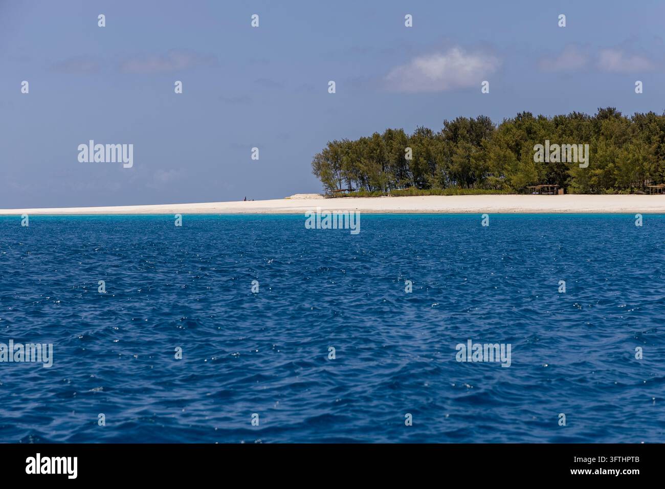 Petite île tropicale avec des arbres verts et une plage de sable blanc vue à travers une mer d'un bleu profond avec des abris en paille sur le rivage, Matemwe, Tanzanie Banque D'Images