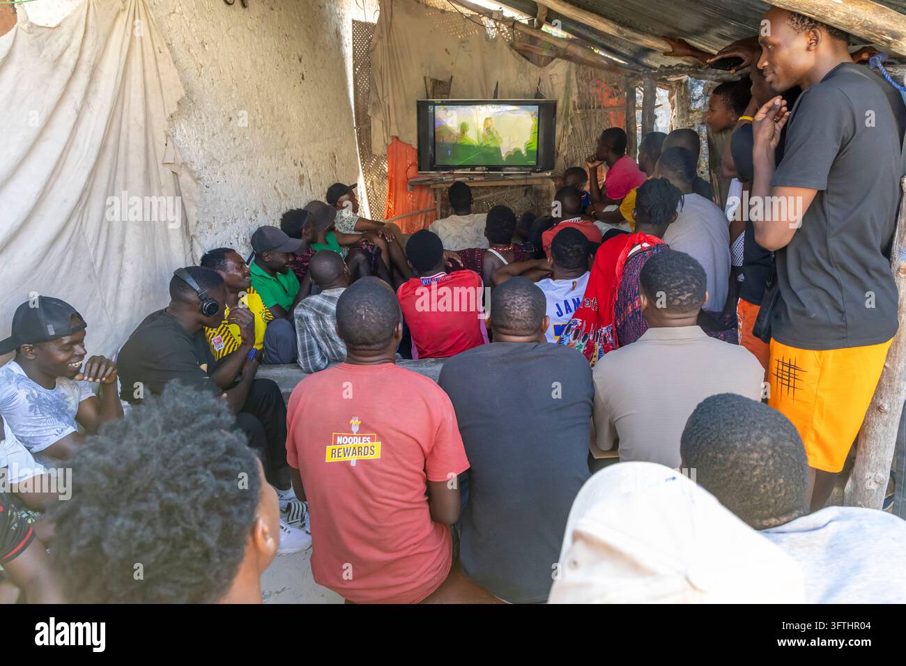 Foule d'hommes regardant le football à la télévision dans un abri rustique en plein air avec un mur en pierre coralline et un toit en tôle ondulée, Jambiani, Tanzanie Banque D'Images