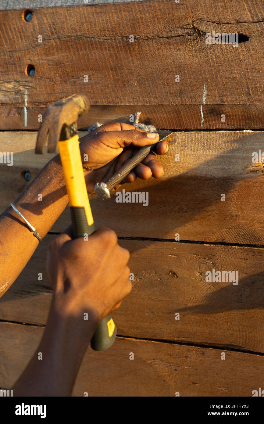Close-up de mains enfonçant un clou dans des planches de bois lors de la construction traditionnelle d'un bateau, Menabe, Belo sur Mer, Madagascar Banque D'Images