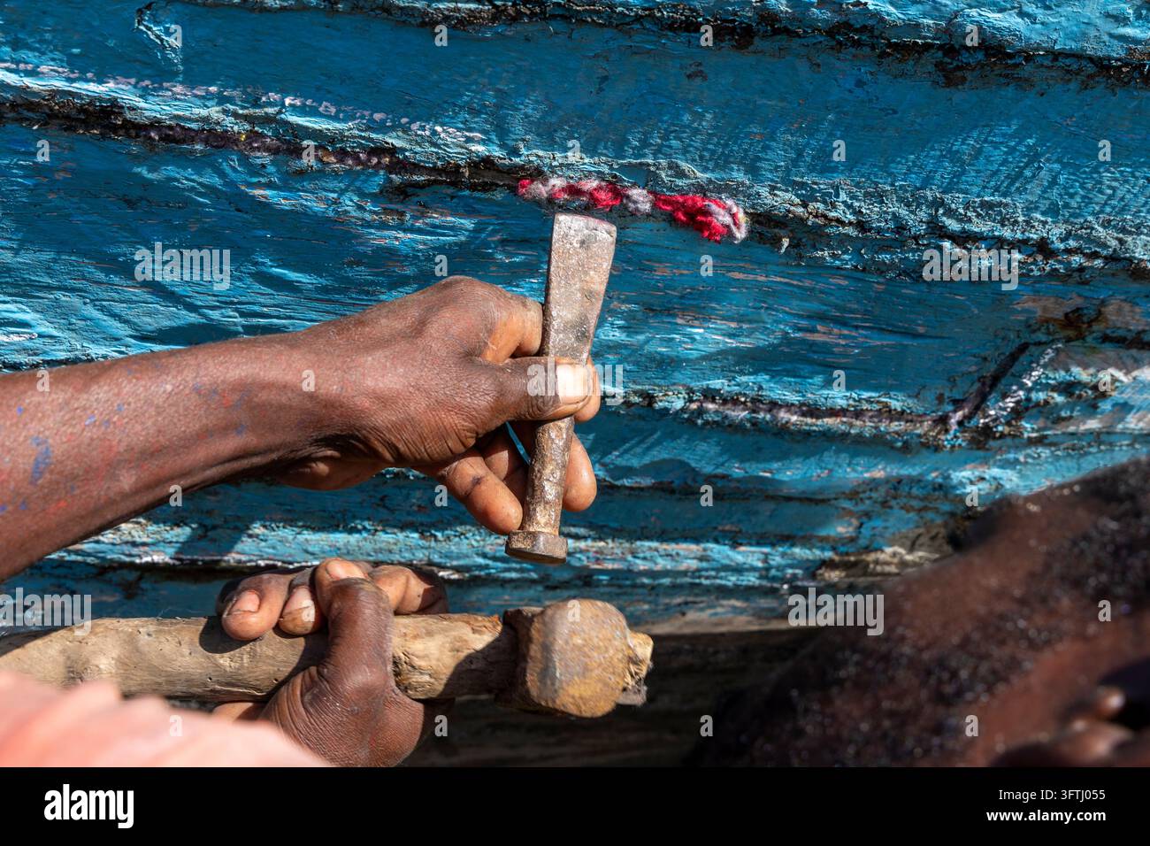 Close-up d'un homme Vezo en train de marteler du matériau de calfeutrage dans les coutures de la coque d'un bateau en bois, Menabe, Belo sur Mer, Madagascar Banque D'Images