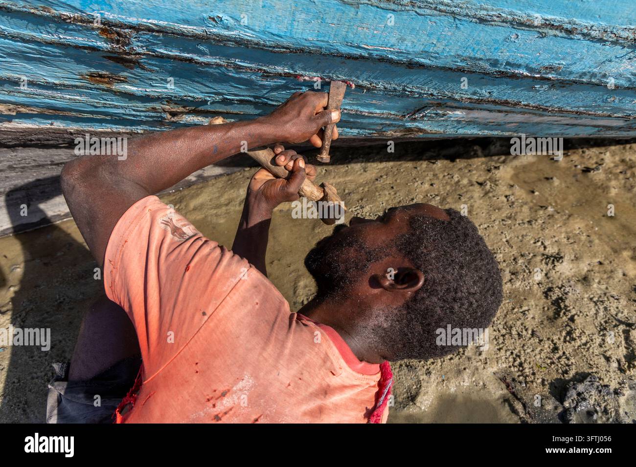 Homme Vezo regardant vers le haut tout en martelant et calfatant la coque en bois d'un bateau de pêche traditionnel, Menabe, Belo sur Mer, Madagascar Banque D'Images