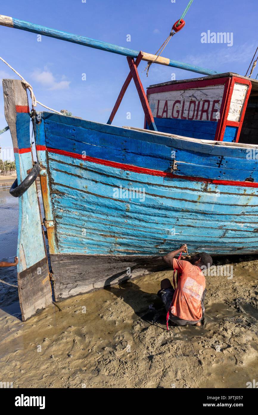 Homme Vezo agenouillé dans la boue en réparant la coque du bateau en bois nommé La Gloire, Menabe, Belo sur Mer, Madagascar Banque D'Images