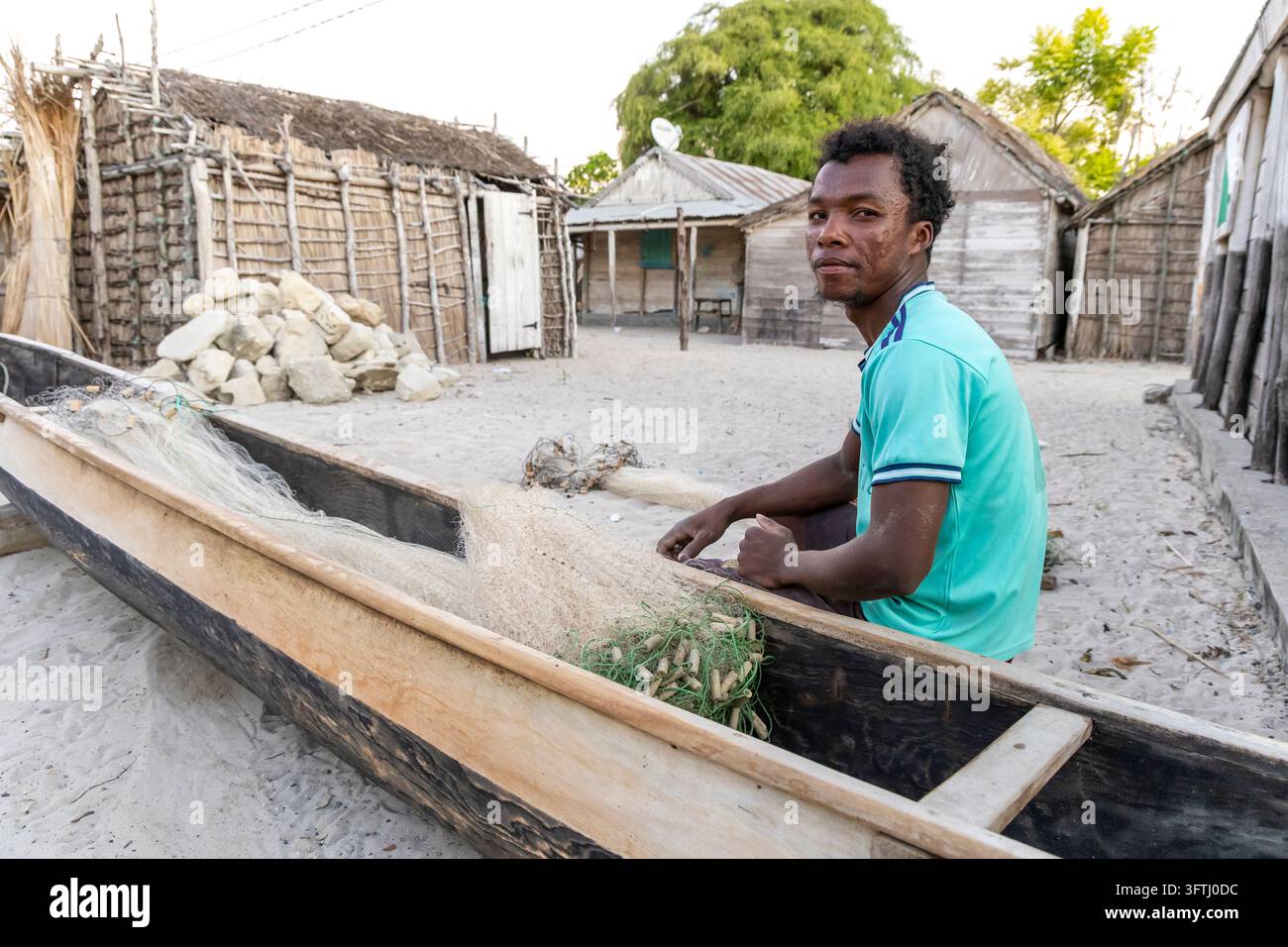 Un pêcheur Vezo est assis dans sa pirogue en bois et répare soigneusement un filet de pêche dans la cour de sable du village, Menabe, Belo sur Mer, Madagascar Banque D'Images