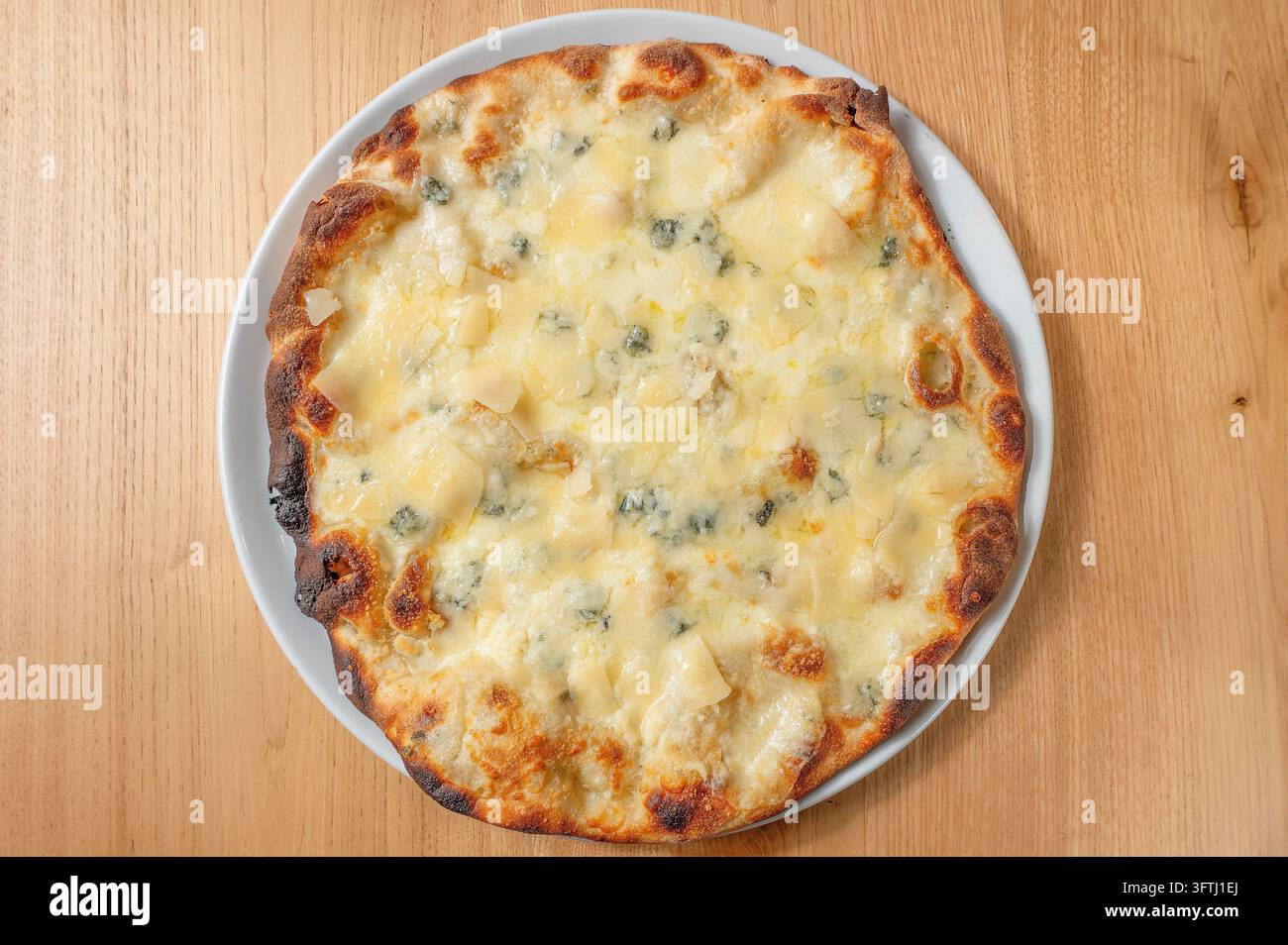Pizza italienne quattro formaggi garnie d'un mélange de fromages fondus, avec une croûte dorée, servie sur une assiette blanche sur une table en bois. Banque D'Images