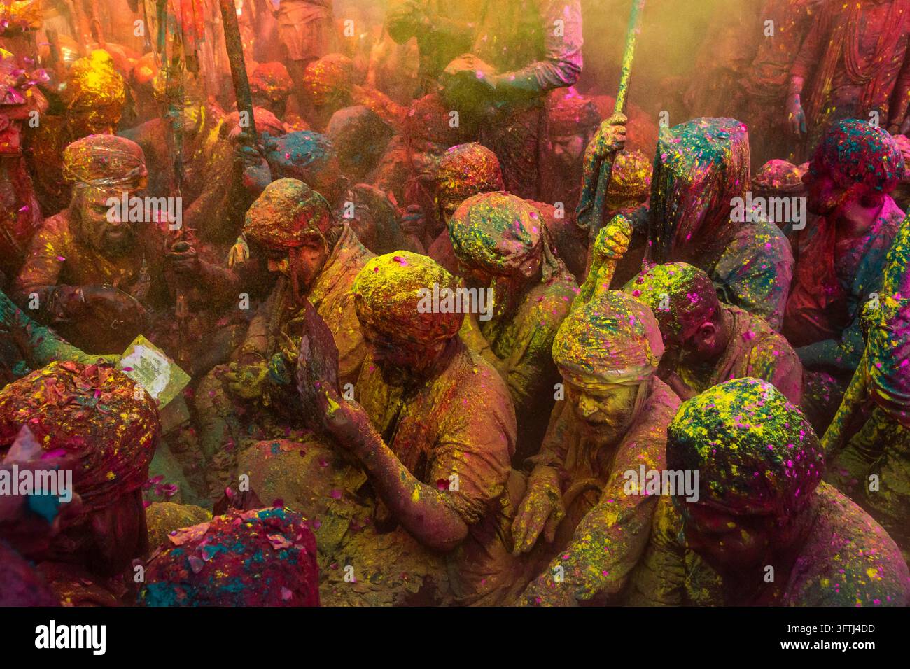 Hommes avec des bâtons de lathi assis dans de la poudre colorée à Braj Ki Holi, Nandgaon, Uttar Pradesh, Inde Banque D'Images