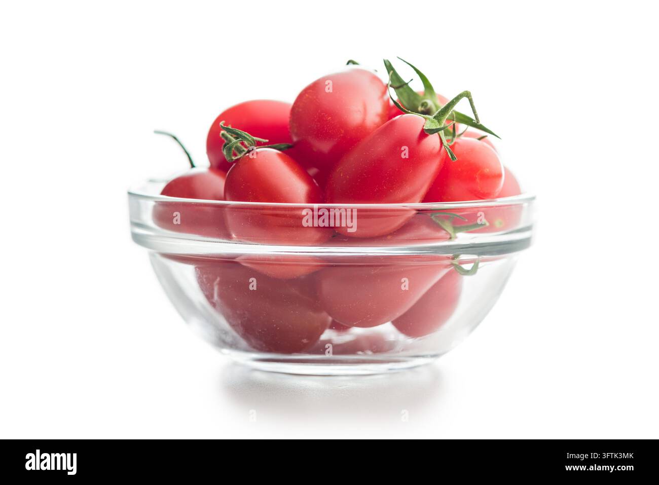 Tomates cerises rouges fraîches empilées dans un bol en verre transparent sur un fond blanc, parfaites pour les recettes, les ingrédients de salade, une alimentation saine, les plats végétariens, le stylisme alimentaire et la photographie culinaire en studio. Banque D'Images