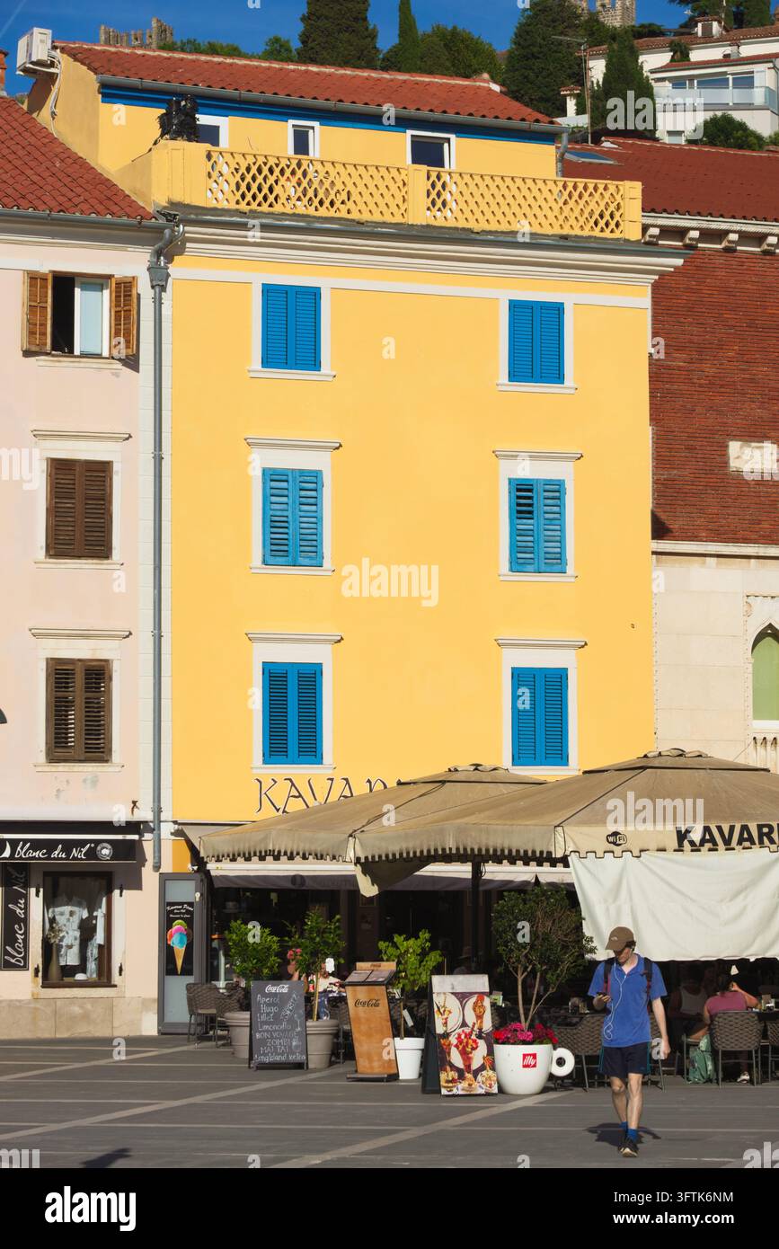 Façade jaune vif avec volets bleus au-dessus d’un parasol de café en terrasse sur la place Tartini dans la ville côtière de Piran, en Slovénie. Banque D'Images