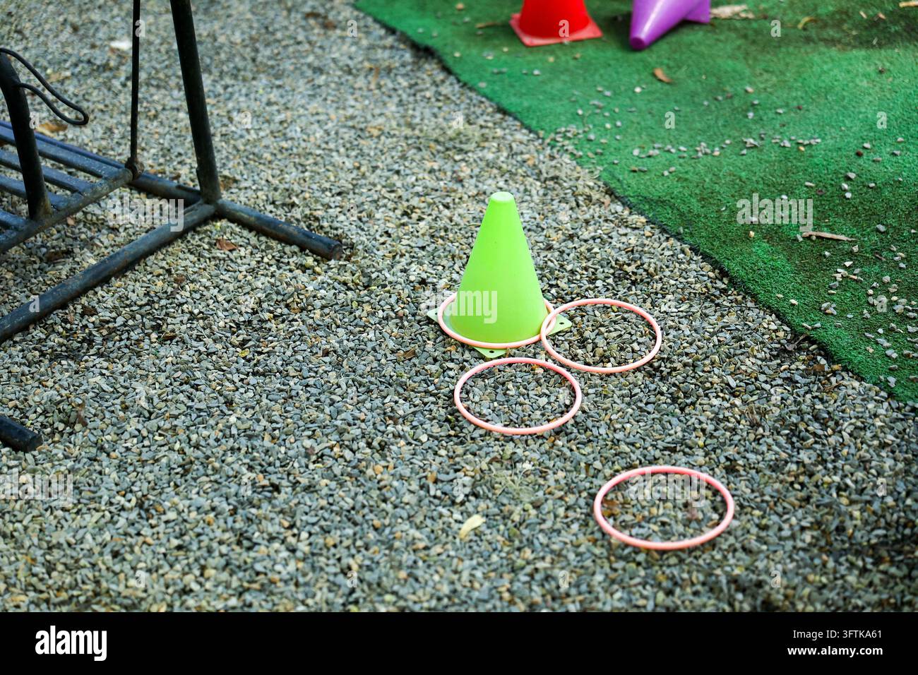 Un jeu de lancer d'anneaux coloré avec un cône vert sur une surface de gravier à côté de la pelouse synthétique, créant une scène de loisirs extérieurs ludique pour les enfants et Banque D'Images
