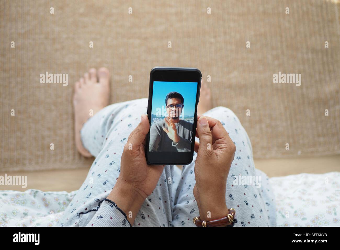 Une femme est assise sur un lit et tient un smartphone pendant un appel vidéo Banque D'Images