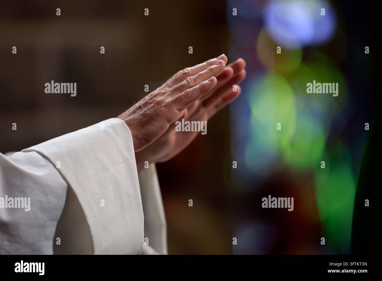 Les mains d'un prêtre vêtu d'une aube blanche font un geste de bénédiction pendant une messe catholique. Banque D'Images