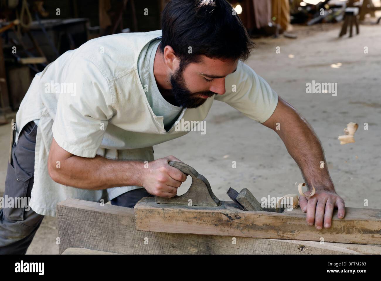 Chantier médiéval au château de Guédelon. Un charpentier vêtu d'une tenue médiévale plane soigneusement une longue planche de bois. Treigny, France. Banque D'Images