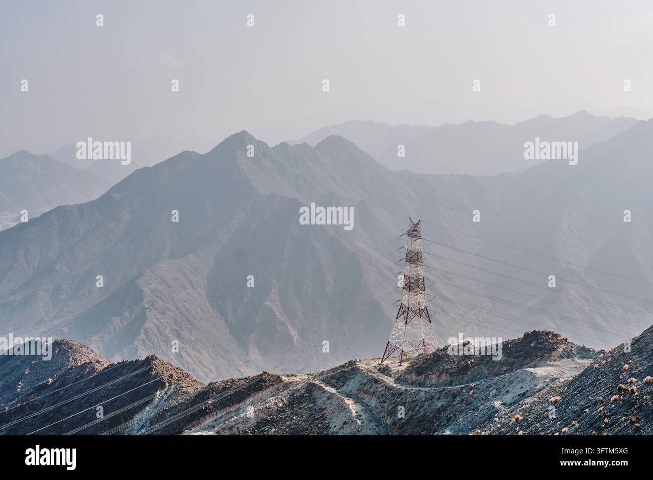 Pylône électrique se dressant sur les pics rocheux accidentés des montagnes Hajar près de Khor Fakkan, Émirats arabes unis. Infrastructure énergétique, distribution d'énergie et technologie a Banque D'Images