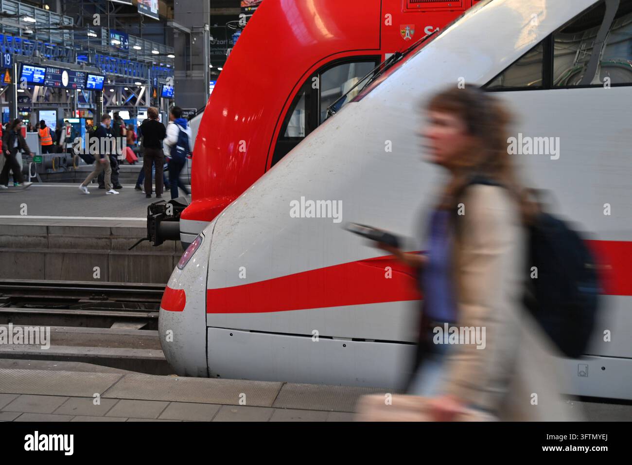 Photo sur le thème Deutsche Bahn DB. Une passagère qui passe, floue par le mouvement, devant l'avant d'un train express ICE à la gare centrale de Munich. *** Photo mise en avant : Deutsche Bahn DB  Une passagère qui passe, floue par le mouvement, devant l'avant d'un train express ICE à la gare centrale de Munich Banque D'Images