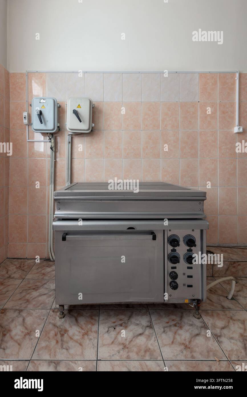Une plaque de cuisson électrique commerciale avec four et plaques chauffantes solides est posée contre un mur de cuisine carrelé avec espace libre au-dessus Banque D'Images