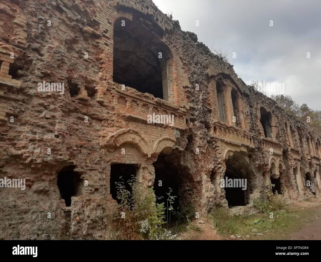 Long bâtiment en maçonnerie en ruine avec des ouvertures en arc vides et des murs rugueux Banque D'Images